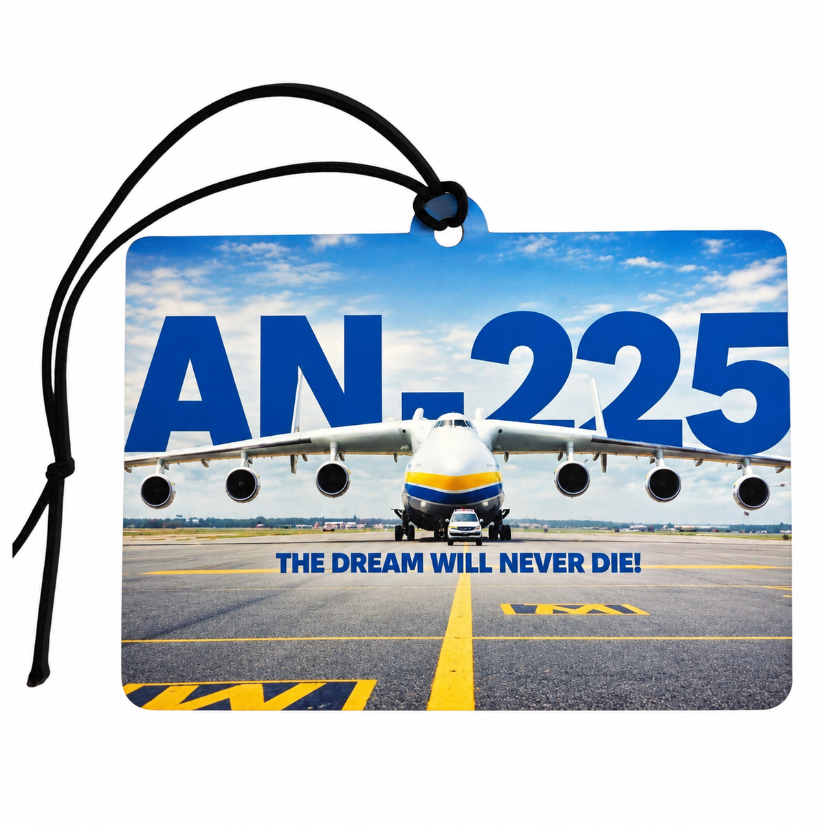 A rectangular printed luggage tag or car air freshener tag with a black hanging cord, featuring a large printed photo of an Antonov An-225 transport aircraft on an airport runway under a blue sky. The text 'AN-225' and 'THE DREAM WILL NEVER DIE!' are printed on the tag.
