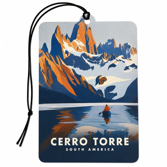 A rectangular luggage tag or car air freshener tag with a black hanging cord, featuring a stylized travel poster design of Cerro Torre in South America. The graphic shows orange and blue mountain peaks, snowy slopes, a reflective lake, and a small canoe with a person.