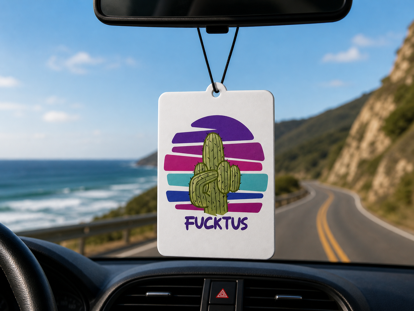 Car air freshener with a cactus design hanging from a car's rearview mirror, with a scenic road and ocean view outside.