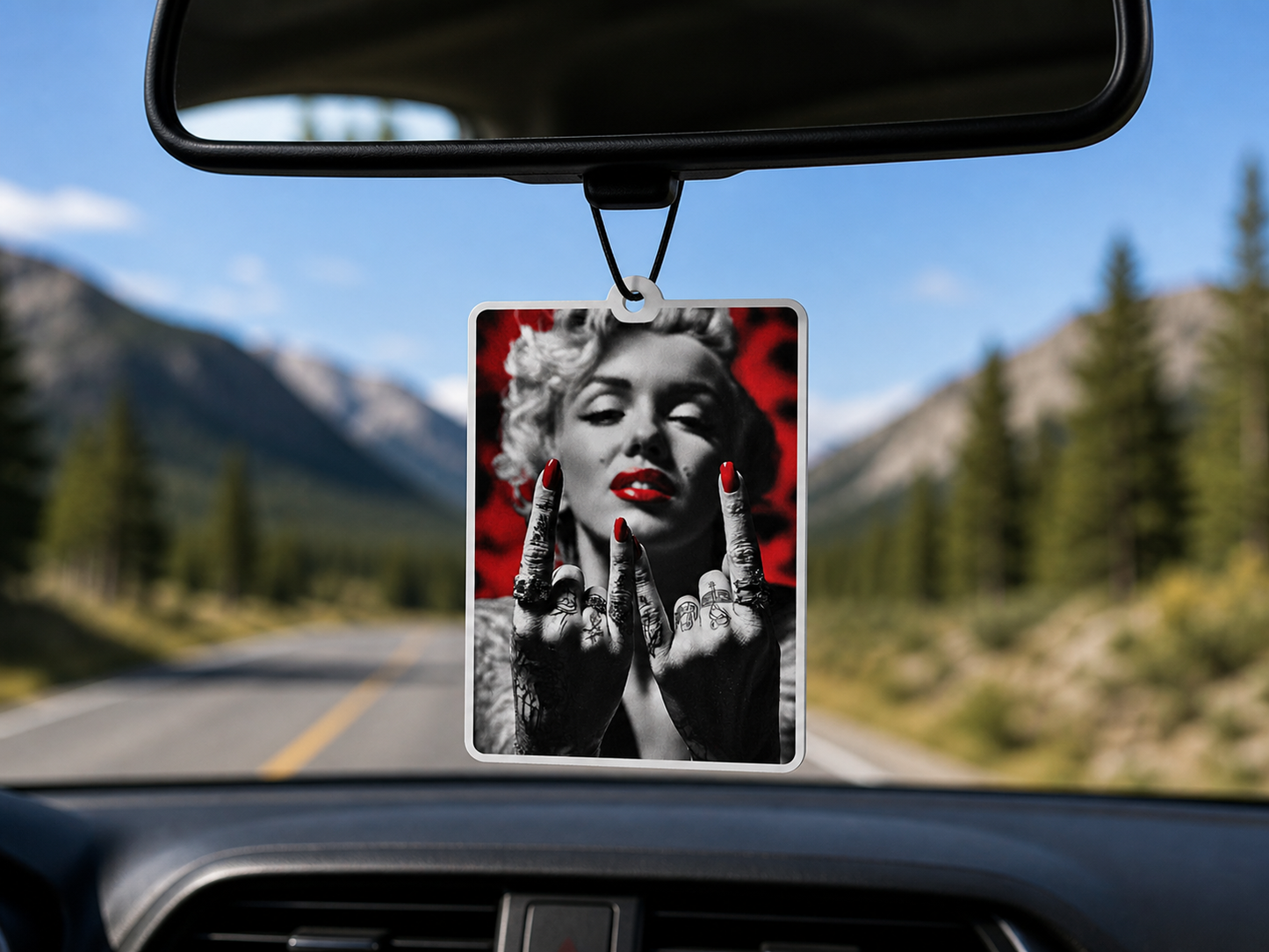 Car air freshener with a stylized portrait of a famous actress hanging from a car's rearview mirror with a scenic road and mountains in the background.