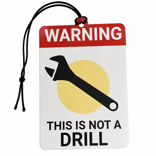 A novelty warning tag-shaped car air freshener or ornament with a black hanging cord. The tag features a red header with the word 'WARNING' in white, a black wrench graphic over a yellow circle, and the text 'THIS IS NOT A DRILL' in black on a white background.